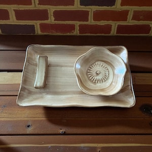 May include: A light brown, wooden serving set featuring a rectangular tray with a handle and a small, flower-shaped bowl. The tray and bowl have a natural wood grain pattern and a glossy finish. The set is designed for serving appetizers or snacks.