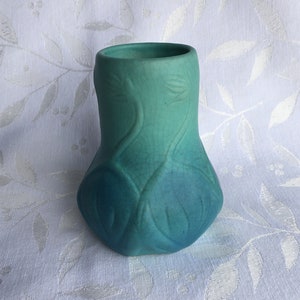 May include: A teal blue ceramic vase with a unique, organic design. The vase has a rounded, bulbous shape and a smooth, glazed finish.