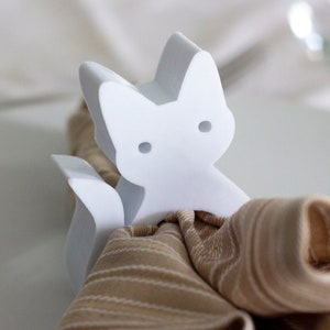 May include: White ceramic napkin ring shaped like a cat with a brown and white striped napkin.