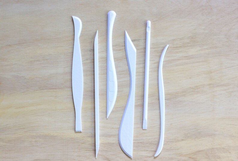 May include: Set of seven white plastic sculpting tools for crafting and modeling clay. The tools have different shapes and sizes, including a curved blade, a pointed tool, and a flat tool.
