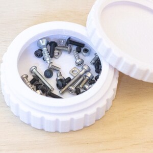 May include: A white plastic container with a lid, filled with various screws, bolts, and washers.
