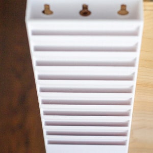 May include: White plastic card holder with 12 slots and three holes at the top.