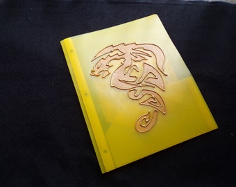 May include: A yellow plastic folder with a copper-colored dragon design. The folder has three holes for a binder.