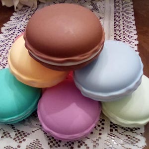 Puede incluir: Seis macarons de color pastel apilados uno encima del otro. Los macarons son en tonos de azul claro, verde claro, rosa claro, amarillo claro y marrón.
