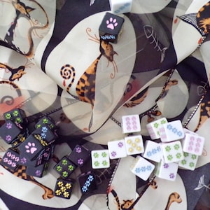 May include: A collection of colourful dice with paw prints on each side, scattered on a white and black fabric with a cat print.