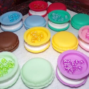 May include: Assortment of colorful macarons with various toppings, including sprinkles, beads, and small candies. The macarons are arranged on a white surface.