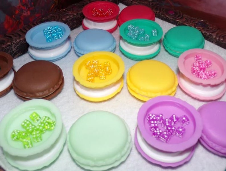 May include: Assortment of colorful macarons with various toppings, including sprinkles, beads, and small candies. The macarons are arranged on a white surface.