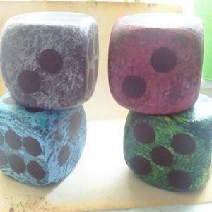 May include: Four painted dice, each with a different color and number of black dots. The dice are stacked in two pairs, with the top dice in each pair showing a different number of dots.