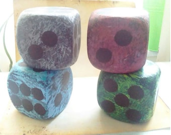 May include: Four painted dice, each with a different color and number of black dots. The dice are stacked in two pairs, with the top dice in each pair showing a different number of dots.
