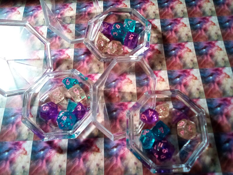 May include: Three clear octagonal containers filled with colorful dice. The dice are translucent and have pink numbers. The dice are in shades of purple, blue, and white.