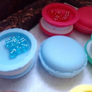 May include: Four colorful macaron-shaped boxes with clear lids. Each box contains small, colorful beads. The boxes are blue, green, pink, and yellow.