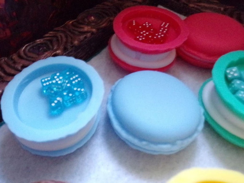 May include: Four colorful macaron-shaped boxes with clear lids. Each box contains small, colorful beads. The boxes are blue, green, pink, and yellow.