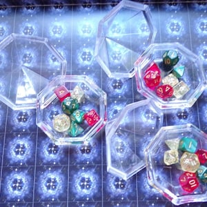 May include: Six clear plastic containers with lids, each containing a set of colorful dice. The dice are red, green, and gold with black numbers.