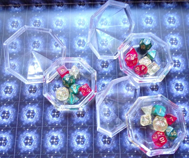May include: Six clear plastic containers with lids, each containing a set of colorful dice. The dice are red, green, and gold with black numbers.