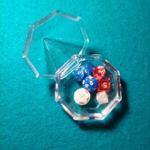 May include: A clear plastic octagonal box with a lid, containing six dice. The dice are red, blue, and white with gold numbers.