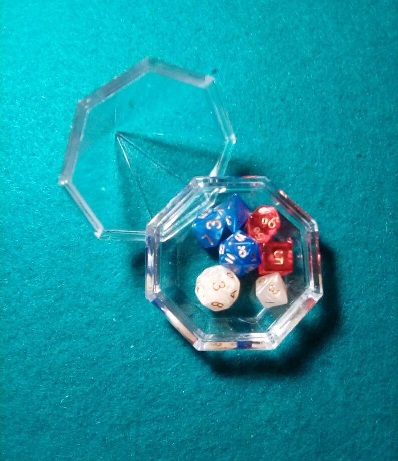 May include: A clear plastic octagonal box with a lid, containing six dice. The dice are red, blue, and white with gold numbers.