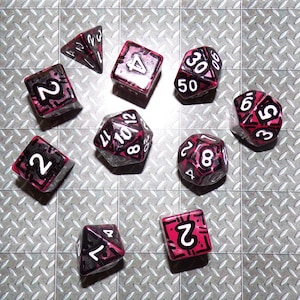May include: A collection of ten polyhedral dice, each with a unique shape and number of sides. The dice are clear with a pink and black design, and white numbers. The dice are arranged on a silver, diamond-plate surface.