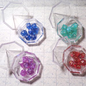 May include: Four sets of polyhedral dice in clear, octagonal containers. The dice are in various colors: blue, green, purple, and red. Each set includes multiple dice for tabletop gaming.