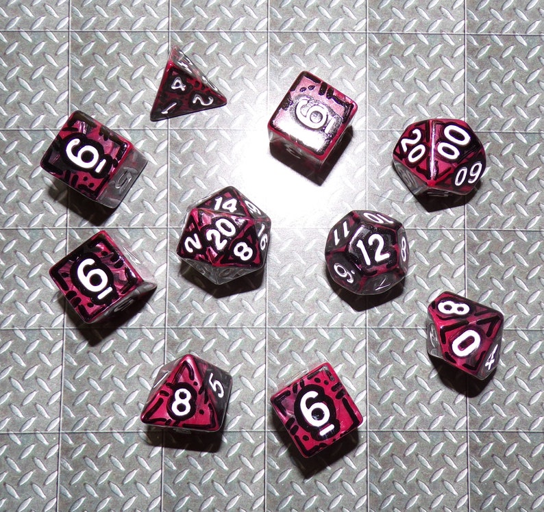 May include: A collection of multi-sided dice in various shapes, including a tetrahedron, cube, and icosahedron. The dice are primarily black with red accents and white numbering. The dice are arranged on a textured, metallic surface.