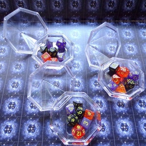 May include: Four clear plastic octagonal boxes with lids, each containing a set of colorful dice with black and gold numbers. The dice are in various shapes and sizes.