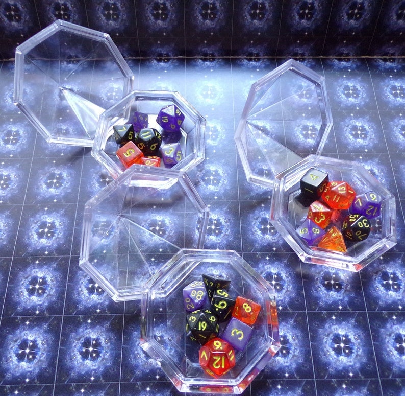 May include: Four clear plastic octagonal boxes with lids, each containing a set of colorful dice with black and gold numbers. The dice are in various shapes and sizes.