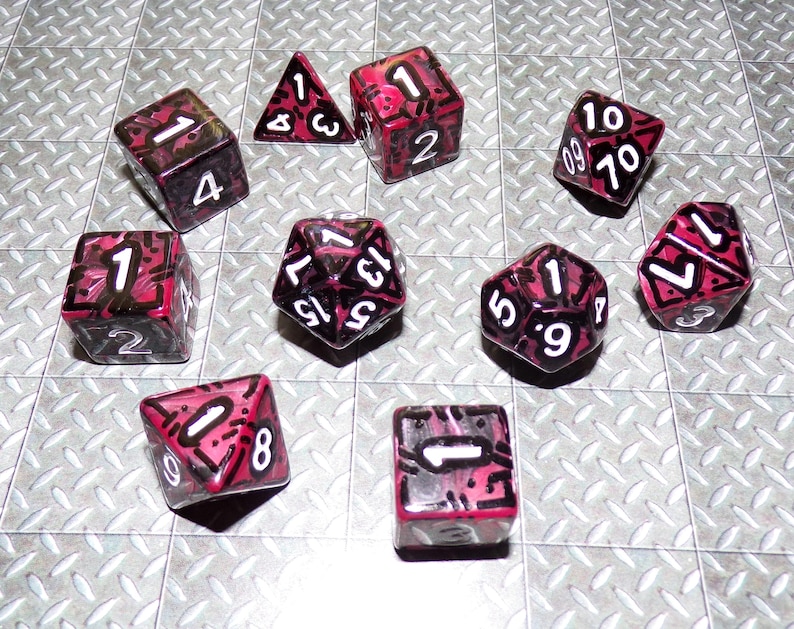 May include: A collection of ten polyhedral dice in various shapes, including a triangular prism, cubes, and a dodecahedron. The dice are transparent with a red and black design and white numbers. The dice are for tabletop games.