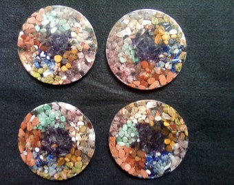May include: Four round coasters with a variety of colorful stones embedded in clear resin. The stones are a mix of green, blue, purple, red, and brown.