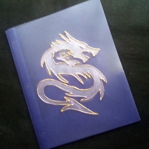 May include: A purple notebook with a silver dragon design on the front cover.
