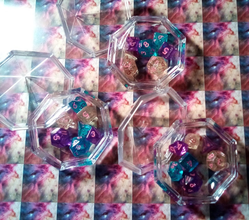 May include: A set of six clear plastic containers with lids, each containing a collection of colorful dice. The dice are a mix of purple, blue, and pink with white numbers.