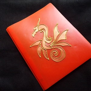 May include: A red notebook with a gold metallic design of a stylized dragon on the front cover.