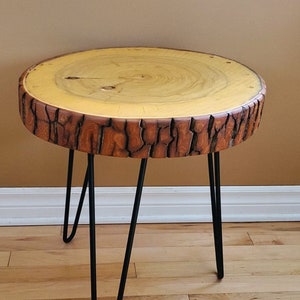 May include: A round side table with a natural wood top and a dark brown, textured edge. The table has three black hairpin legs. The wood top is approximately 51 cm in diameter.