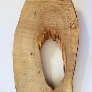 May include: A large, oval-shaped piece of wood with a natural, light brown colour. The wood has a large, oval-shaped hole in the centre.