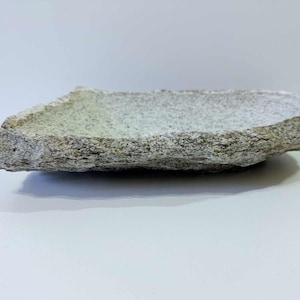 Peut inclure: Un plat en pierre naturelle avec un extérieur rugueux et texturé et une couleur gris clair. Le plat a une forme rectangulaire avec des bords irréguliers et repose sur une surface blanche. Ce plat décoratif en pierre est idéal pour servir des aliments.