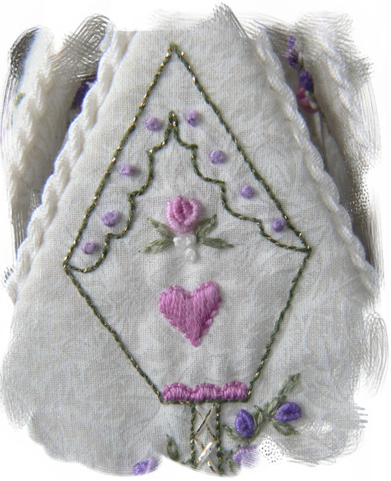 May include: White fabric with a green and gold embroidered design. The design features a heart, a flower, and a series of small dots.