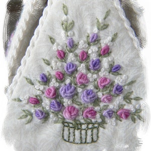 May include: A white fabric with a hand-stitched design of a basket of purple and pink flowers. The flowers are embroidered with white beads.