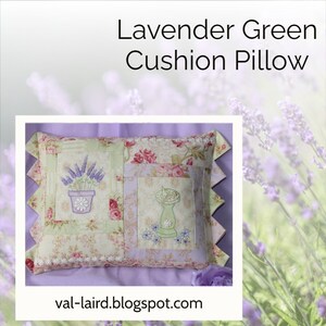 Puede incluir: Una almohada de color verde lavanda con un diseño de patchwork que presenta flores de lavanda bordadas en una maceta y un bebedero para pájaros. La almohada tiene un borde festoneado y se muestra sobre una superficie morada.