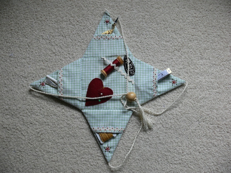 Peut inclure: Une trousse de couture en forme d'&eacute;toile en tissu vichy bleu et blanc avec un c&oelig;ur rouge, des bobines de fil et une aiguille. La trousse est attach&eacute;e avec un cordon blanc.