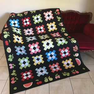 May include: A black quilt with a patchwork design featuring colorful squares and a watermelon pattern. The quilt is decorated with green leaves and red cherries.