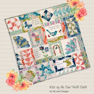 May include: A colourful quilt with a patchwork design featuring various floral patterns and quotes. The quilt is titled "Kiss of the Sun Wall Quilt" by Val Laird Designs.