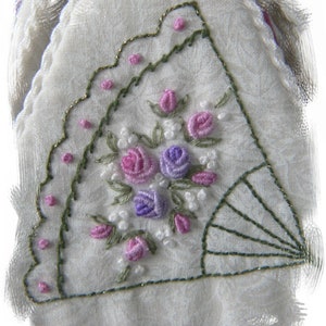 May include: A white fabric handkerchief with a delicate floral embroidery design. The embroidery features pink, purple, and white flowers with green leaves. The handkerchief has a scalloped edge.