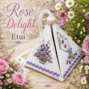 Puede incluir: Un estuche de tela blanco en forma de pirámide con intrincados bordados florales de rosas moradas y rosas, un cordón para colgar con una cuenta moteada y un borde de cinta en zigzag morada. El texto Rose Delight Etui está impreso arriba a la izquierda.