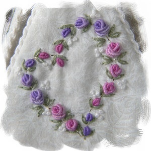 May include: A white fabric with a heart-shaped design embroidered with purple, pink, and green flowers.