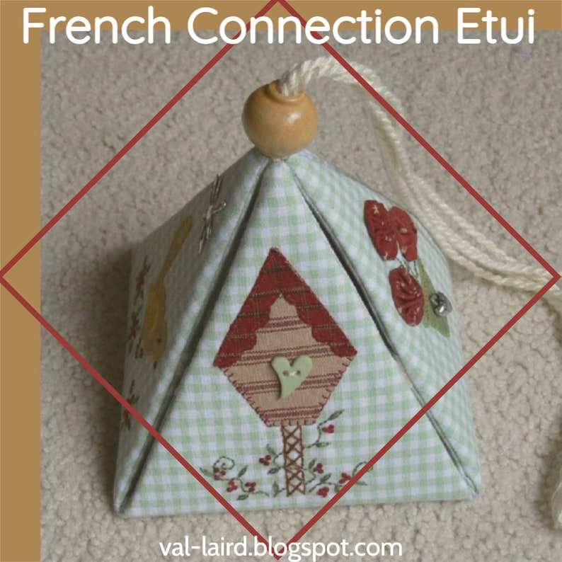 Peut inclure: Une bo&icirc;te en forme de pyramide en tissu vichy vert et blanc avec un motif de nichoir rouge et blanc. La bo&icirc;te est munie d'un cordon blanc attach&eacute; au sommet et est d&eacute;cor&eacute;e de fleurs brod&eacute;es et d'un c&oelig;ur.