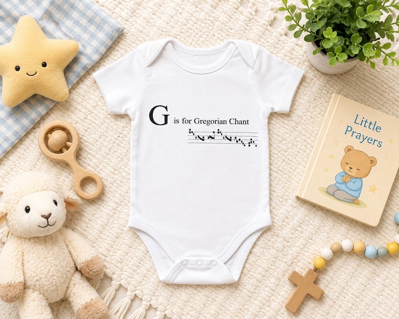May include: White baby onesie with the text "G is for Gregorian Chant" and musical notes. A plush star, wooden rattle, stuffed lamb, small potted plant, and a "Little Prayers" book are also visible.