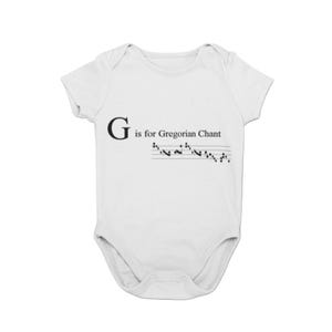 May include: White baby bodysuit with the text "G is for Gregorian Chant" in black. Below the text is a musical staff with notes. The bodysuit is a one-piece garment with short sleeves.