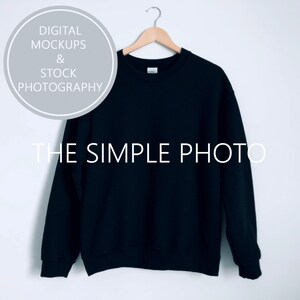 May include: A black crew neck sweatshirt hanging on a wooden hanger against a white background. The sweatshirt is blank and ready for customization.