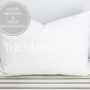 May include: White pillow on a white wooden surface. The pillow is a standard size and has a smooth, white fabric cover. The text "THE SIMPLE PHOTO" is printed in white on the front of the pillow.