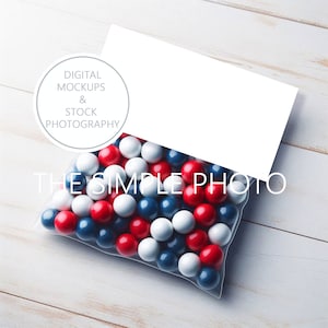 May include: A clear plastic bag filled with red, white, and blue gumballs. The bag is sitting on a white wooden surface. The text "THE SIMPLE PHOTO" is visible on the bag.
