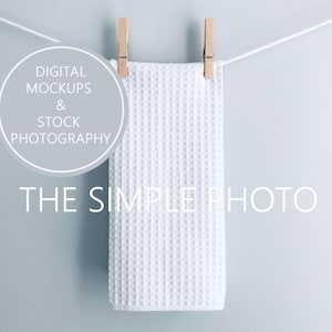 May include: A white waffle weave kitchen towel hanging on a clothesline with wooden clothespins. The towel is against a light blue background. The text "DIGITAL MOCKUPS & STOCK PHOTOGRAPHY THE SIMPLE PHOTO" is visible in the image.