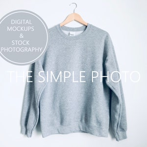 May include: A gray sweatshirt hanging on a wooden hanger against a white background. The sweatshirt has a crew neck and long sleeves.